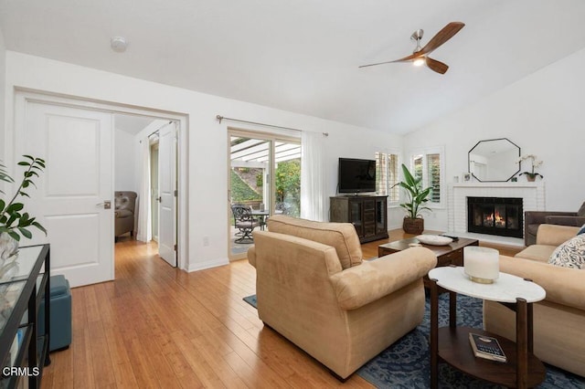 living area featuring baseboards, lofted ceiling, ceiling fan, light wood-style floors, and a fireplace