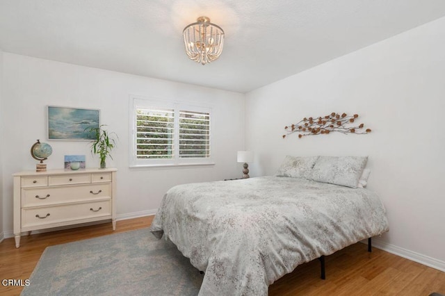 bedroom featuring an inviting chandelier, baseboards, and wood finished floors