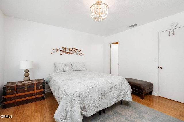 bedroom featuring wood finished floors, visible vents, and a notable chandelier