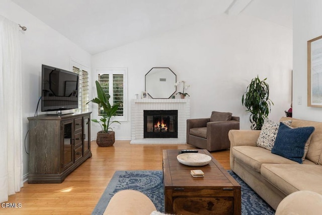 living room with lofted ceiling with beams, light wood finished floors, and a fireplace