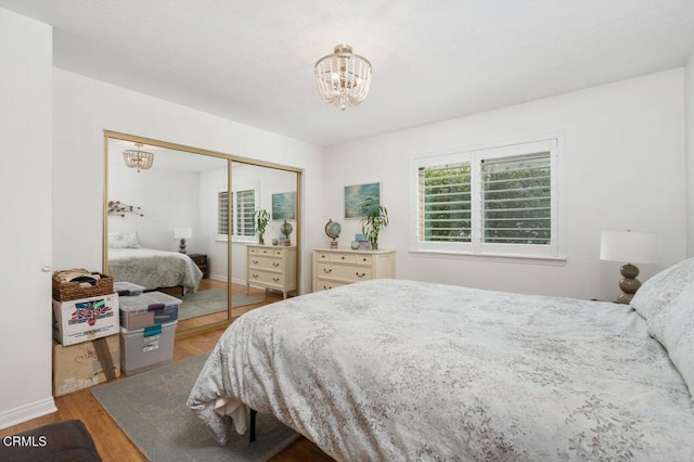 bedroom with baseboards, a closet, a chandelier, and wood finished floors