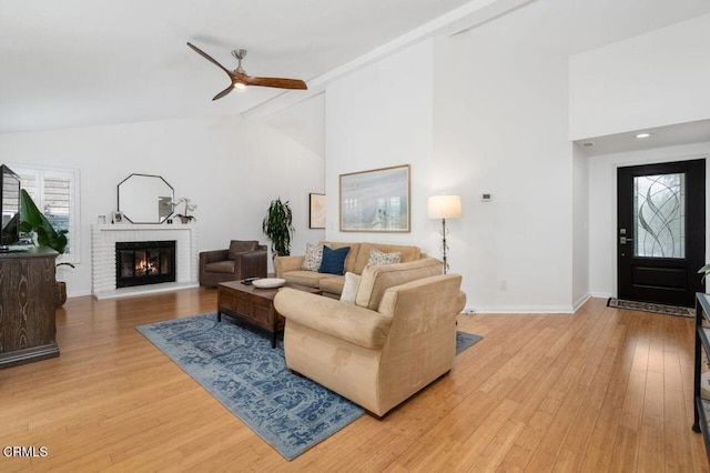 living area with beam ceiling, light wood-type flooring, a brick fireplace, and baseboards