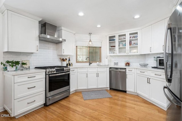 kitchen featuring appliances with stainless steel finishes, wall chimney range hood, white cabinets, a sink, and light countertops