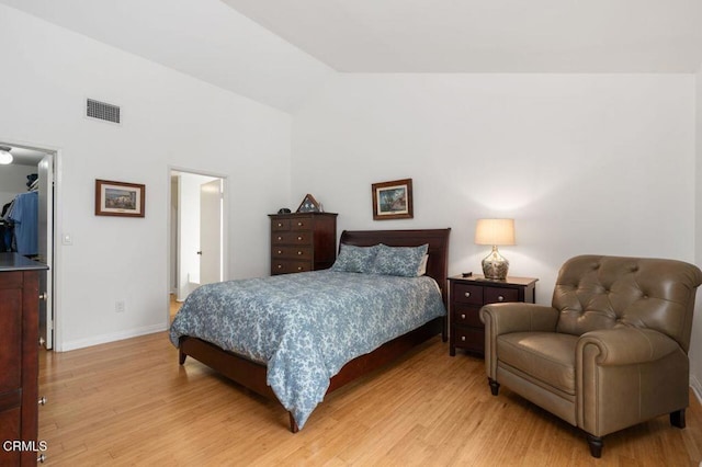 bedroom featuring light wood finished floors, a walk in closet, vaulted ceiling, baseboards, and a closet