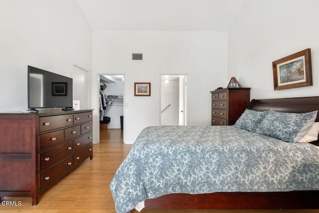 bedroom featuring light wood-type flooring, a spacious closet, a closet, and high vaulted ceiling