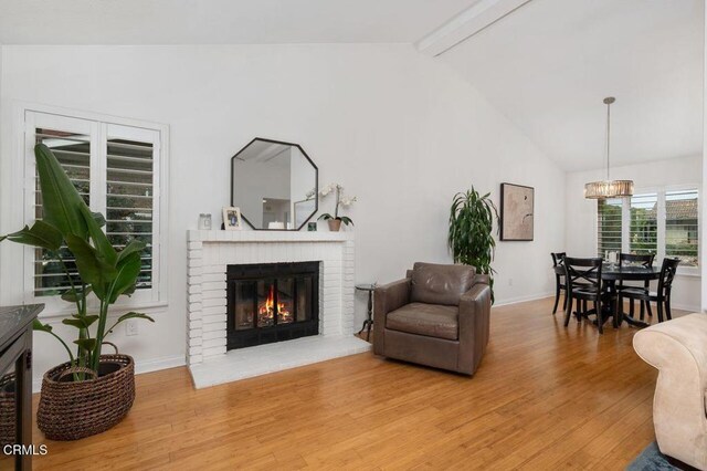 living room featuring light wood finished floors, a brick fireplace, beam ceiling, a chandelier, and baseboards