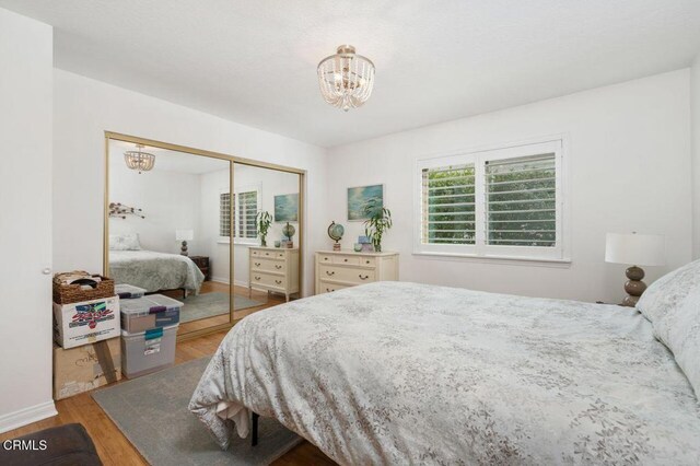 bedroom featuring a chandelier, wood finished floors, a closet, and baseboards