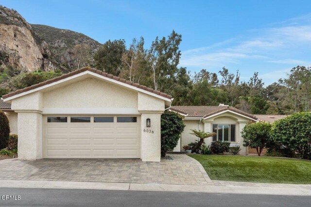 ranch-style house with a tile roof, decorative driveway, stucco siding, and a front lawn