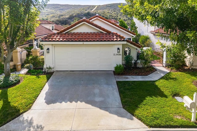 mediterranean / spanish-style home featuring a tile roof, stucco siding, concrete driveway, a gate, and a mountain view