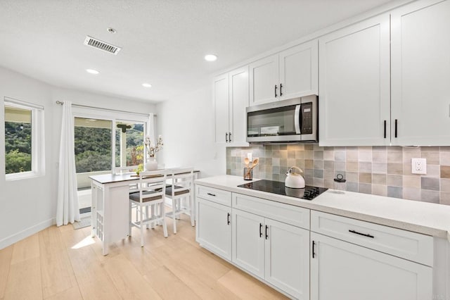 kitchen with light wood finished floors, tasteful backsplash, visible vents, stainless steel microwave, and black electric cooktop