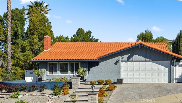 view of front of house featuring a garage, a chimney, decorative driveway, and a tiled roof