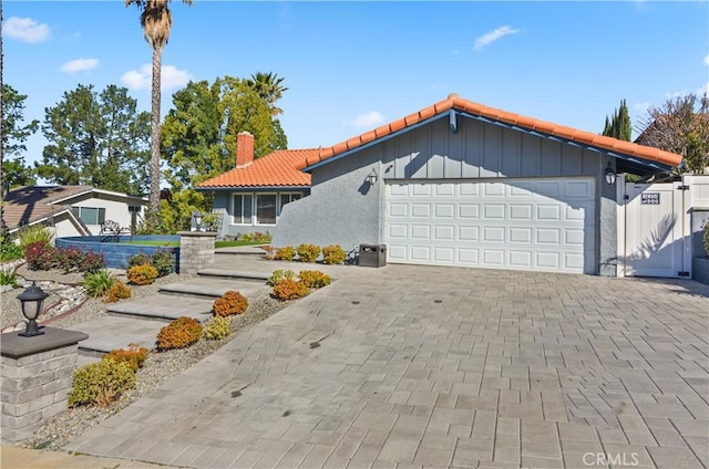 view of front of home with a garage, a tile roof, a chimney, decorative driveway, and stucco siding