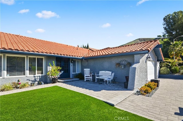 rear view of house featuring a garage, a lawn, a tiled roof, and stucco siding