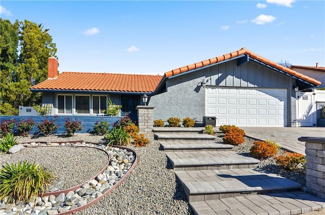 view of front of home featuring a tile roof, a chimney, an attached garage, decorative driveway, and stucco siding