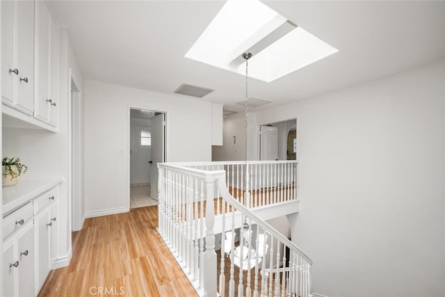 hall featuring visible vents, baseboards, light wood-type flooring, an upstairs landing, and a skylight