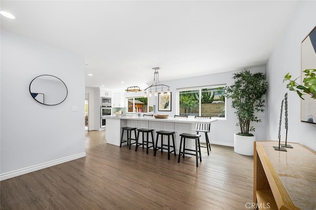 kitchen with stainless steel microwave, white cabinetry, a breakfast bar area, and wood finished floors