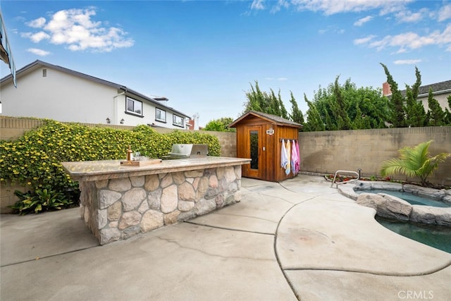 view of patio / terrace with an outbuilding, area for grilling, a fenced backyard, a storage shed, and an in ground hot tub