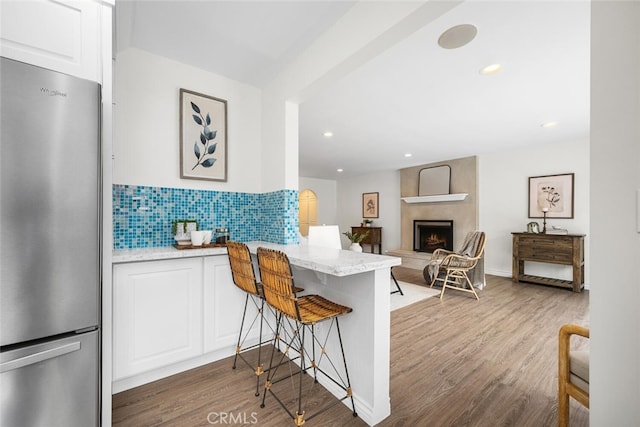 kitchen featuring tasteful backsplash, a fireplace, freestanding refrigerator, wood finished floors, and white cabinets