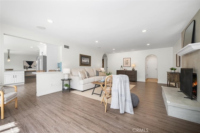 living room with arched walkways, visible vents, recessed lighting, and wood finished floors