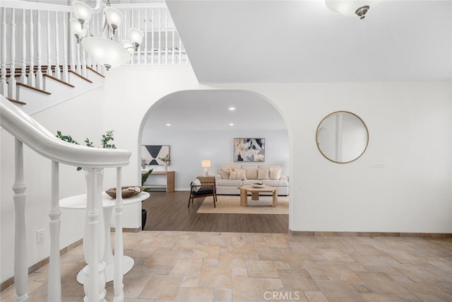 entrance foyer with arched walkways, stairway, stone finish floor, and baseboards