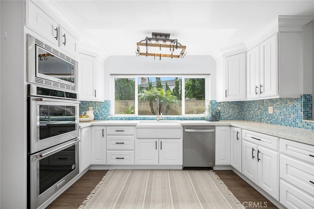 kitchen featuring a sink, backsplash, white cabinets, stainless steel appliances, and dark wood-style flooring