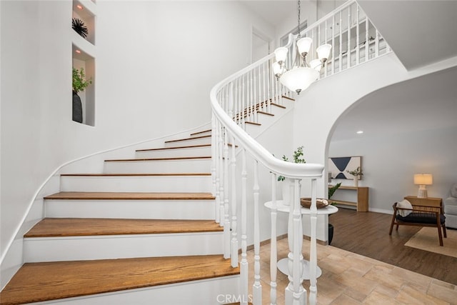 stairs featuring wood finished floors, arched walkways, a chandelier, baseboards, and a towering ceiling