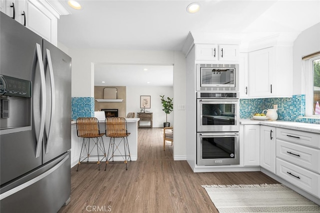 kitchen featuring white cabinets, wood finished floors, tasteful backsplash, and stainless steel appliances