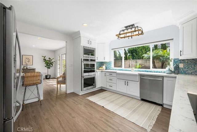 kitchen featuring decorative backsplash, appliances with stainless steel finishes, wood finished floors, white cabinetry, and a sink