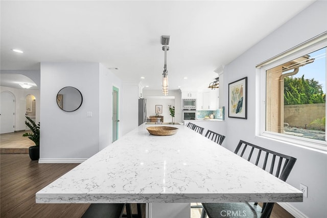 dining area with arched walkways, recessed lighting, baseboards, and dark wood-style flooring