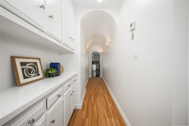 hall featuring arched walkways, baseboards, and light wood finished floors