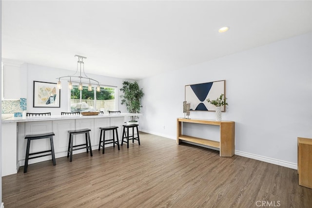 kitchen with wood finished floors, baseboards, white cabinetry, light countertops, and a kitchen bar