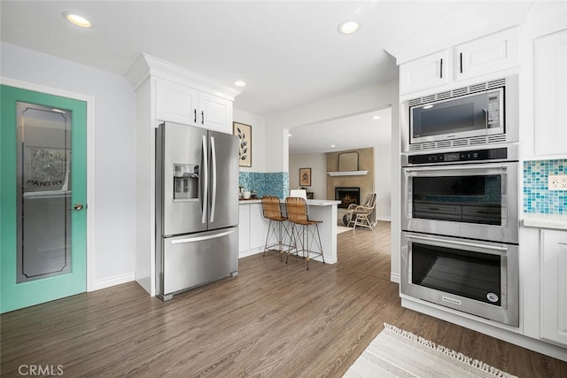 kitchen with backsplash, appliances with stainless steel finishes, wood finished floors, and white cabinets