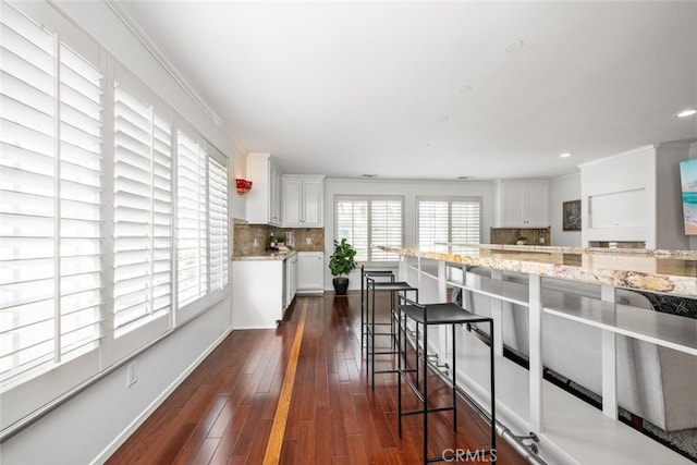 kitchen with a breakfast bar area, ornamental molding, decorative backsplash, white cabinetry, and dark wood-style flooring