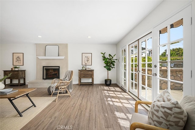 living room featuring wood finished floors, baseboards, recessed lighting, a fireplace with raised hearth, and french doors