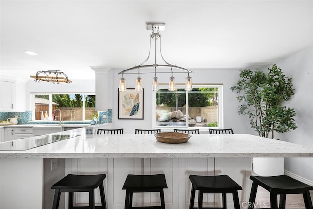 kitchen featuring light stone counters, backsplash, a breakfast bar, and white cabinetry