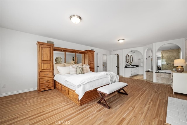 bedroom with arched walkways, light wood-style flooring, and baseboards