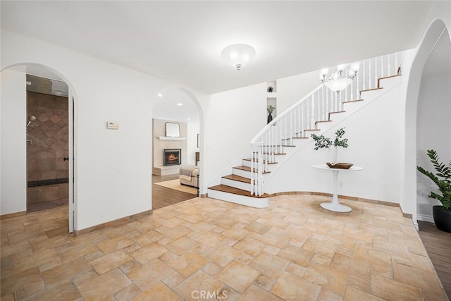 entryway featuring a lit fireplace, stairs, stone finish flooring, and baseboards