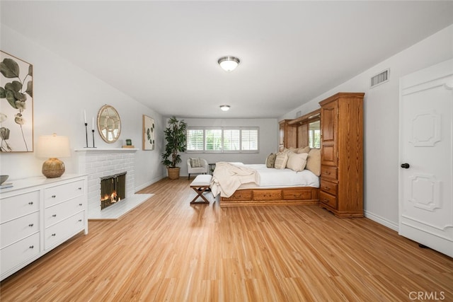 bedroom featuring light wood finished floors, visible vents, a brick fireplace, and baseboards