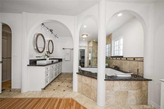 bathroom featuring double vanity, wood finished floors, a garden tub, and a sink