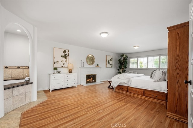 bedroom with a fireplace, light wood-style floors, arched walkways, and baseboards