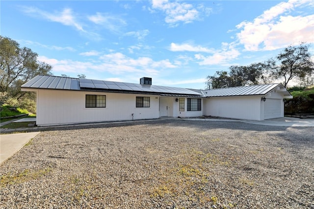 ranch-style home featuring roof mounted solar panels, cooling unit, an attached garage, and metal roof