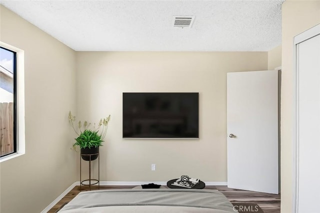 bedroom featuring visible vents, a textured ceiling, baseboards, and wood finished floors