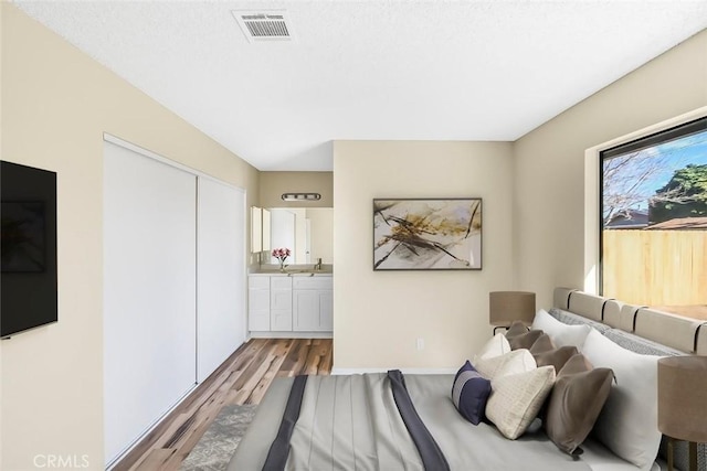 bedroom with a closet, visible vents, light wood-style flooring, and ensuite bath