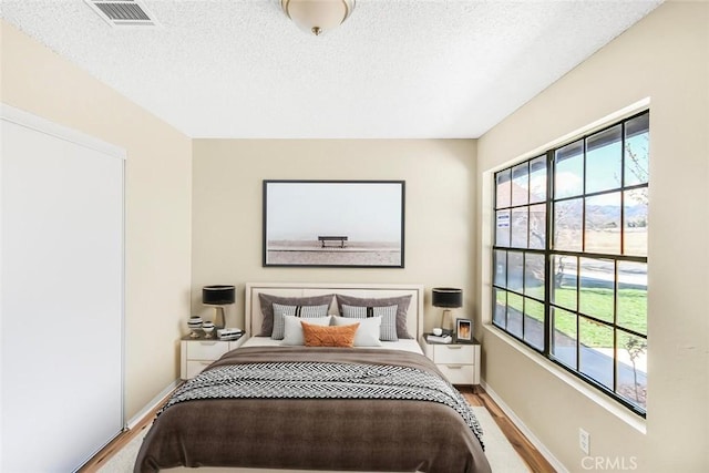 bedroom with multiple windows, visible vents, a textured ceiling, and wood finished floors