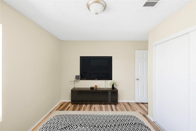 interior space featuring baseboards, a textured ceiling, visible vents, and wood finished floors