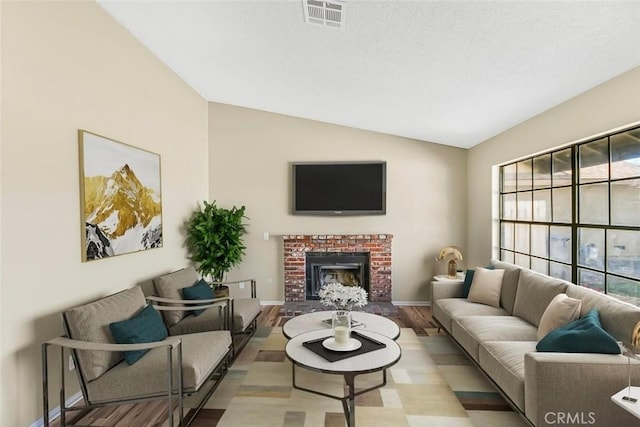 living area with lofted ceiling, visible vents, a brick fireplace, light wood-type flooring, and baseboards