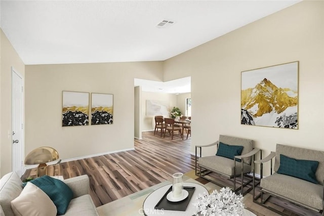 living room with visible vents, vaulted ceiling, baseboards, and wood finished floors