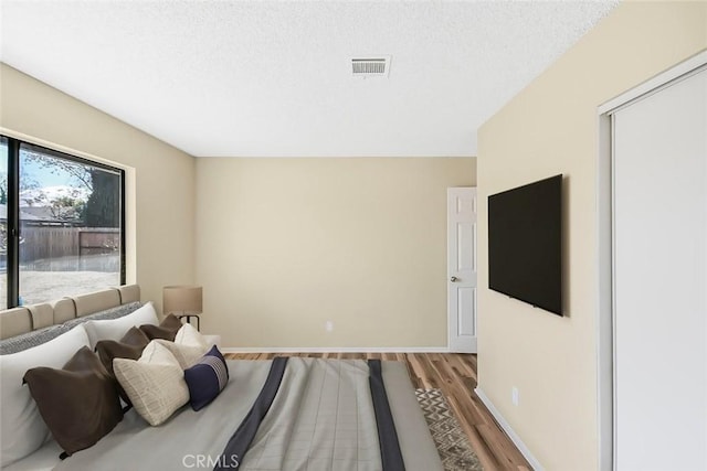 bedroom with a textured ceiling, light wood-type flooring, visible vents, and baseboards