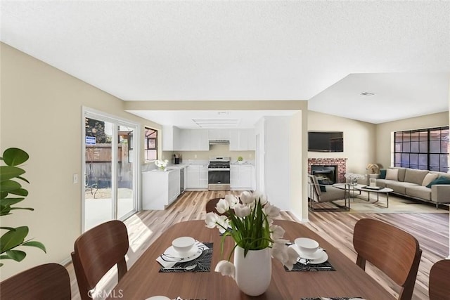 dining room featuring light wood-style floors, a fireplace, and a textured ceiling