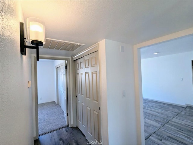 hallway with a textured ceiling, wood finished floors, and visible vents